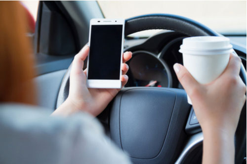 A driver holding a cup and phone, distracted driving lawyer in Delray Beach concept