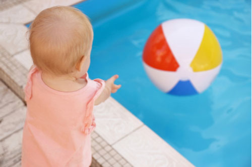 A toddler reaching for a beach ball in a pool